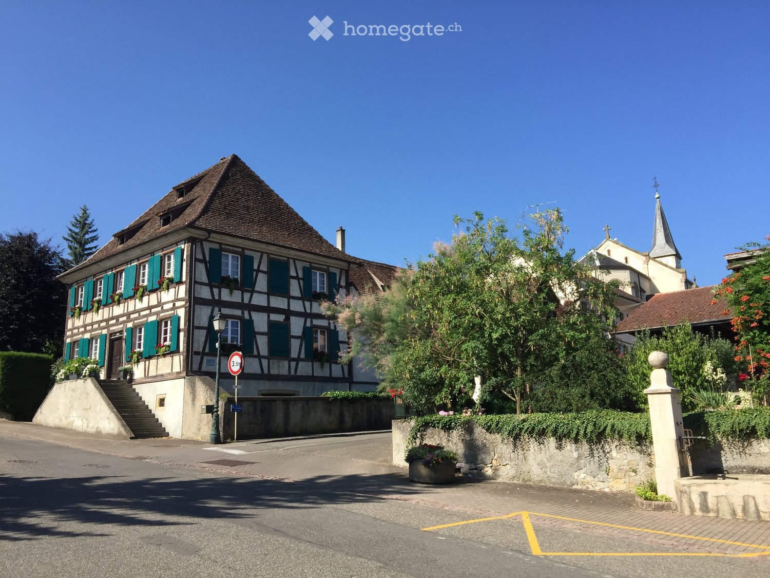 3 story house with a sloped roof, brick and timber facade, stairs, garden with plants and flowers, street light