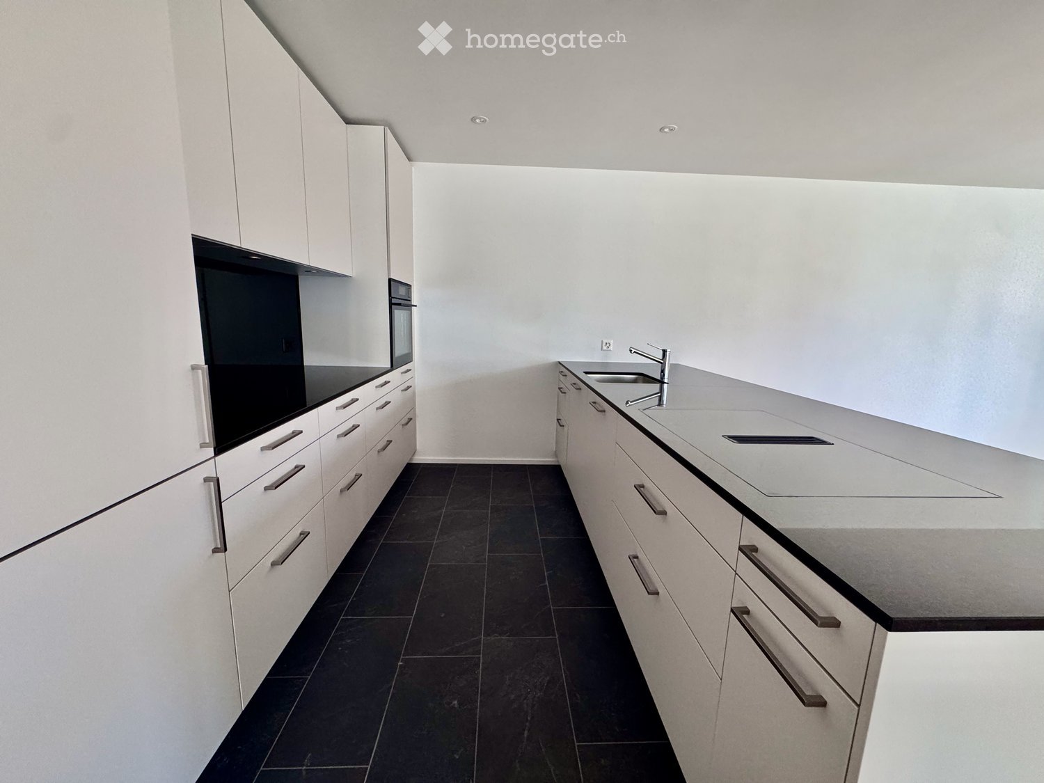 Modern kitchen with white cabinets, dark countertops, and a stainless steel sink.