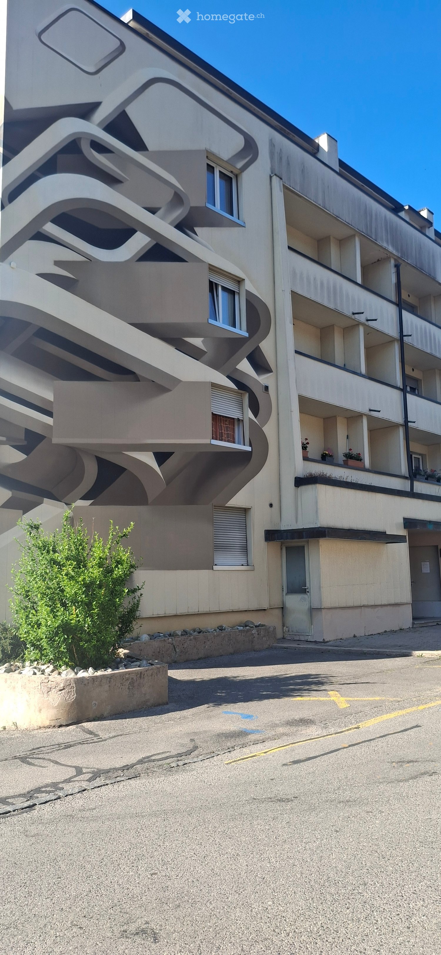 Modern multi-story building with curved balconies and large windows, featuring a small garden area in front.