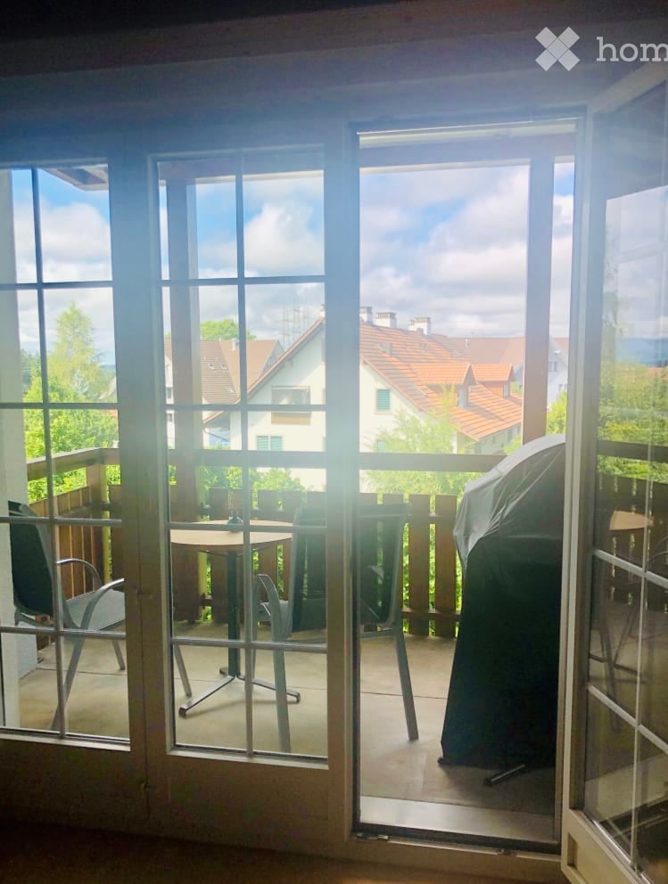 Balcony with a table and chairs, overlooking a residential area with houses and trees.