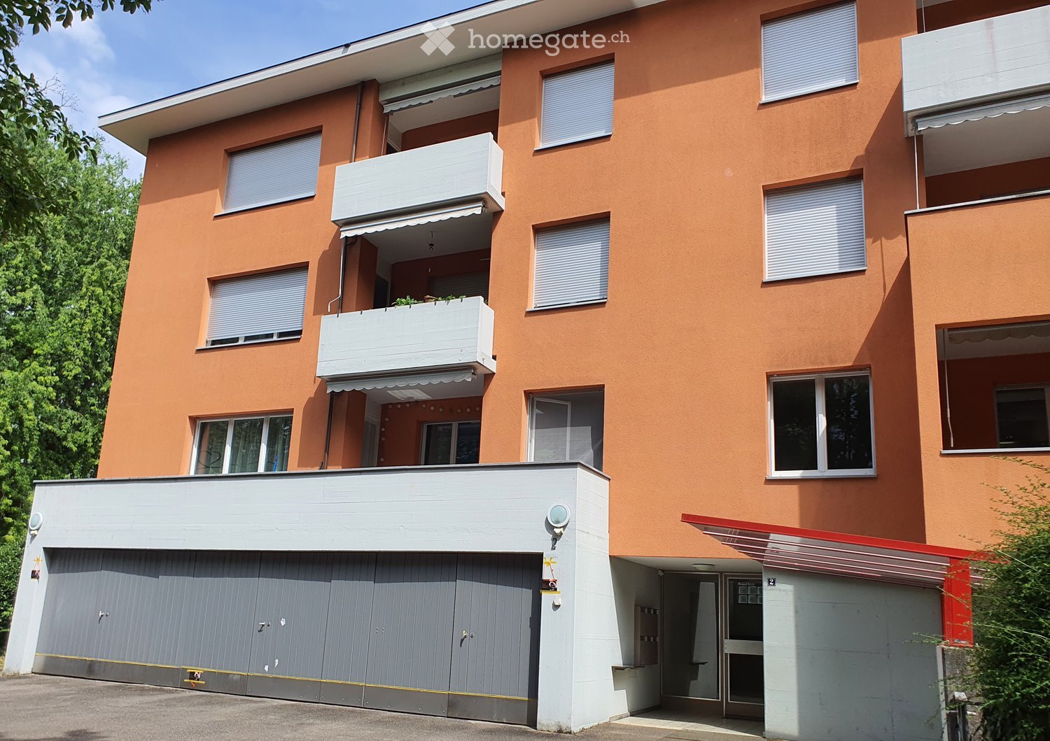 Modern multi-story building with orange facade, white balconies, and a grey garage entrance.