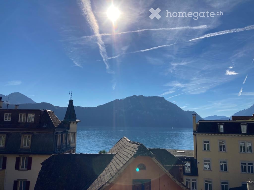 Balcony view overlooking a lake with mountains in the background, featuring several buildings with varied architectural styles.