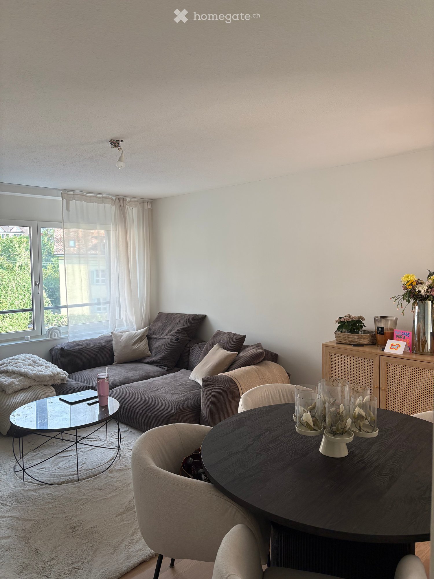 Modern living room with large window, grey sectional sofa, coffee table, side table, decorative vases, and a small cabinet.