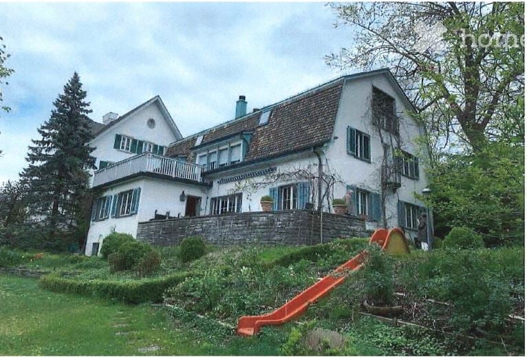 2 story house, white, green window shutters, chimney, small balcony, plants, small slide in front, surrounded by grass