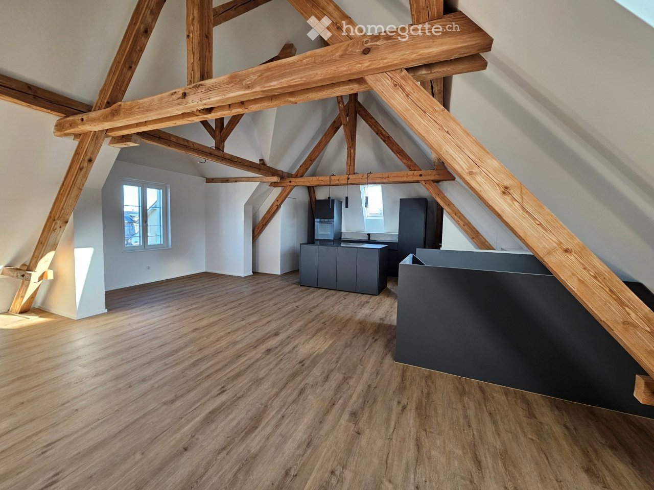 An attic space with exposed wooden beams, wooden flooring, and modern grey cabinets. The room is empty, with no furniture or personal items visible.