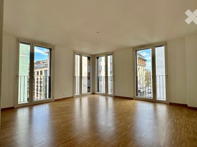 Completely empty room with wooden flooring and large windows with balconies, offering a view of the cityscape.
