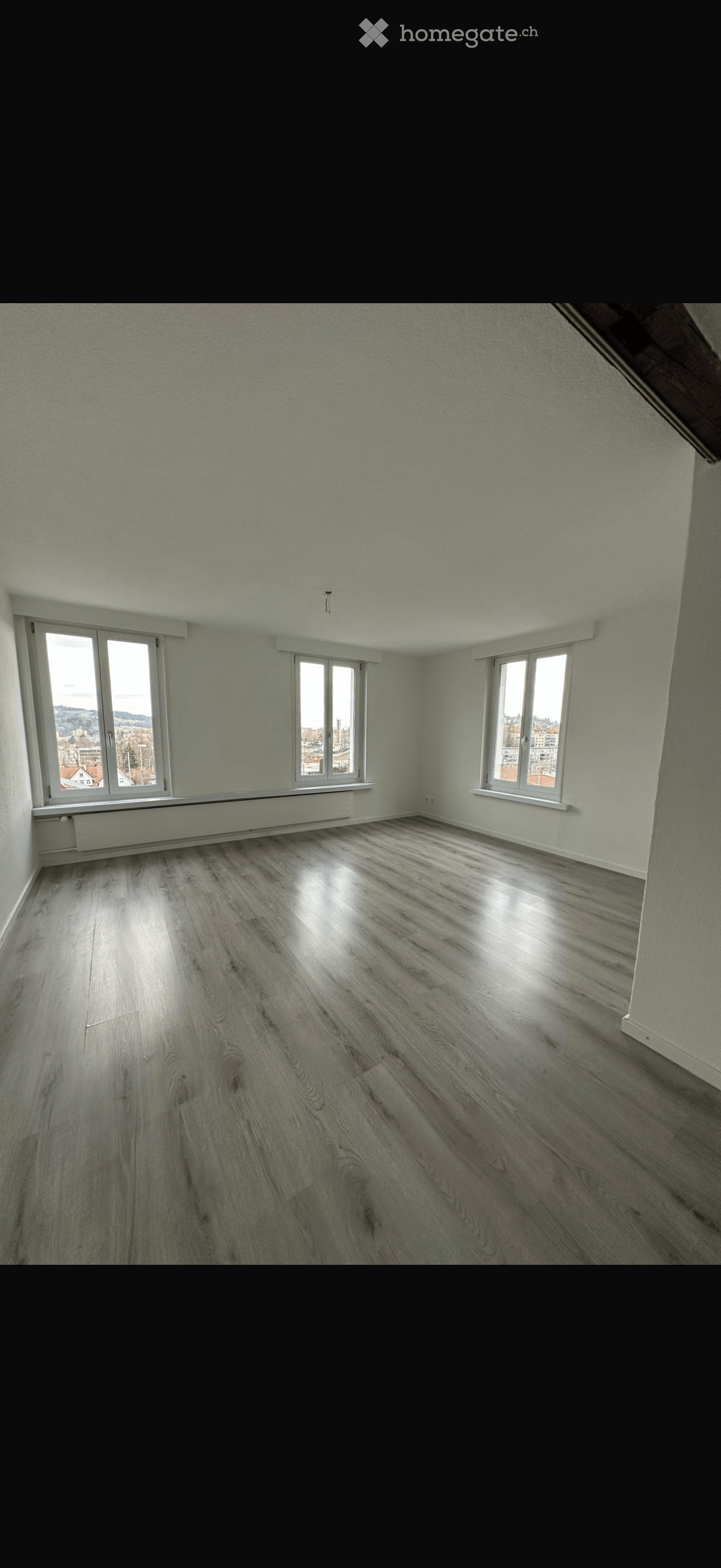 Empty room with light-colored walls, wooden flooring, and multiple windows offering a view of the outside.