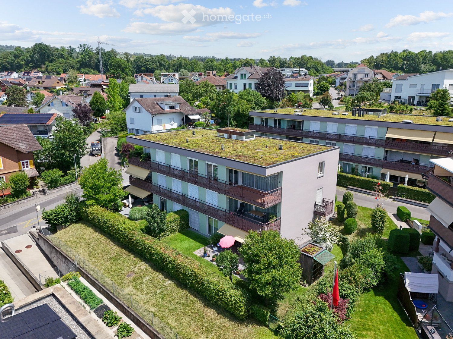 Aerial view of a residential area with multiple buildings, green spaces, and a rooftop garden on one of the structures.