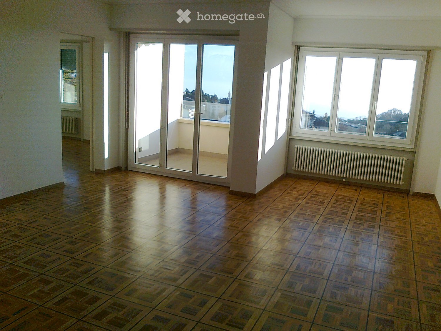 Empty room with wooden flooring, large windows, and a sliding glass door leading to a balcony.