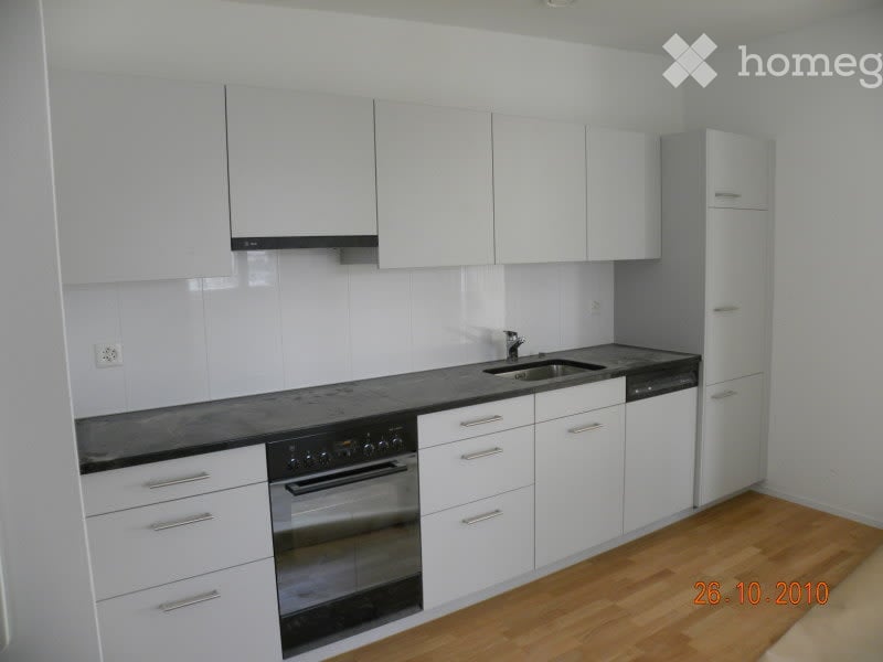 Modern kitchen with white cabinets, black countertops, stainless steel appliances, and wooden flooring.