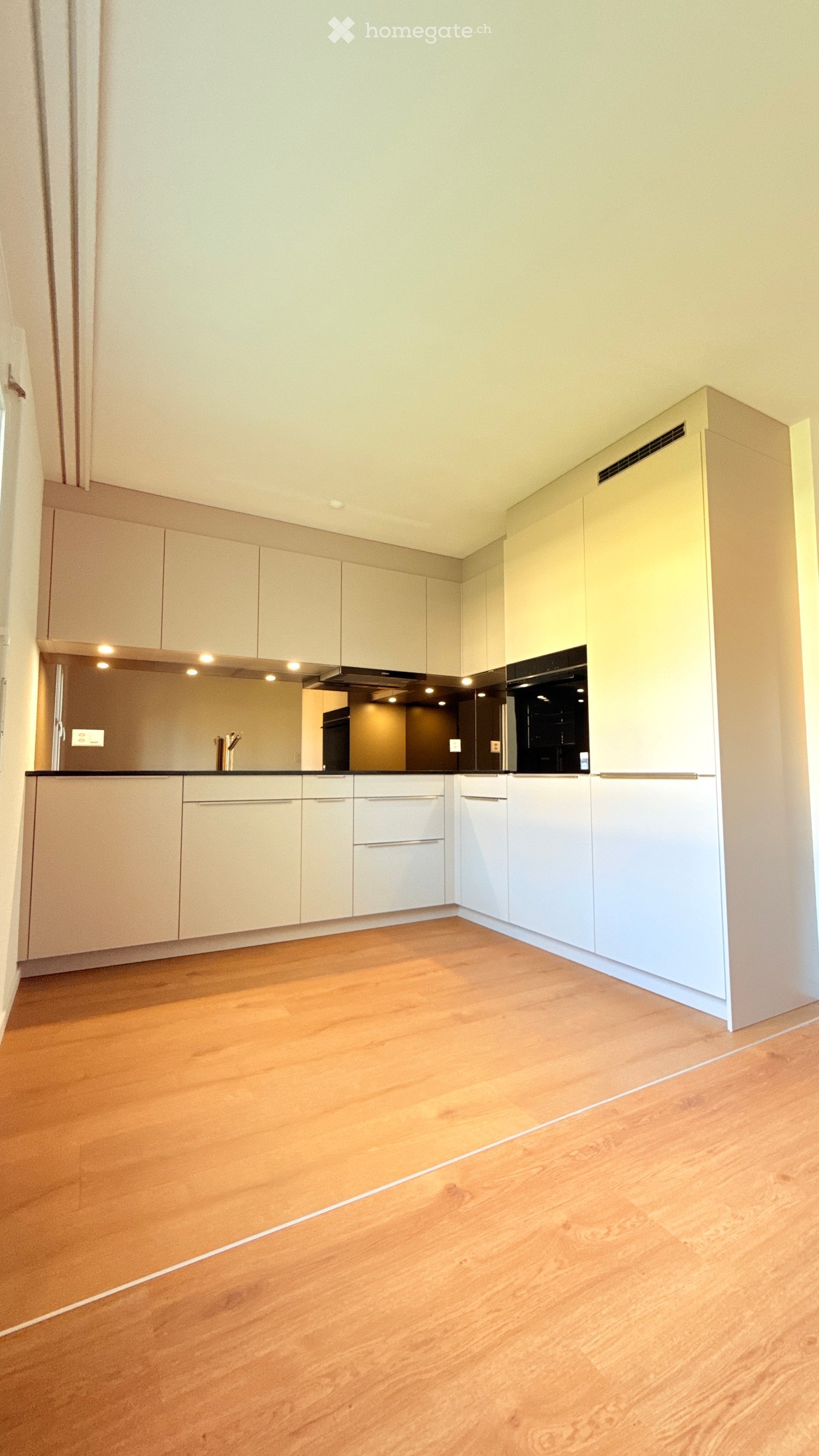 Empty kitchen with light wood cabinets, white countertops, and a wooden floor. No appliances or furniture are present.