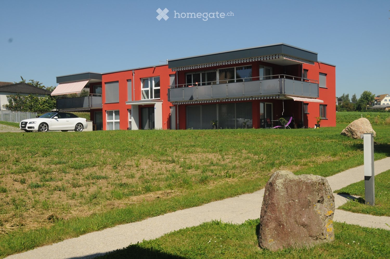 two story house, red brick, white windows, balcony, garage, car parked outside, lawn