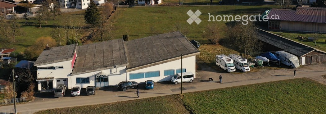 Aerial view of a commercial building with multiple parking spaces, several vehicles, and a few trailers.