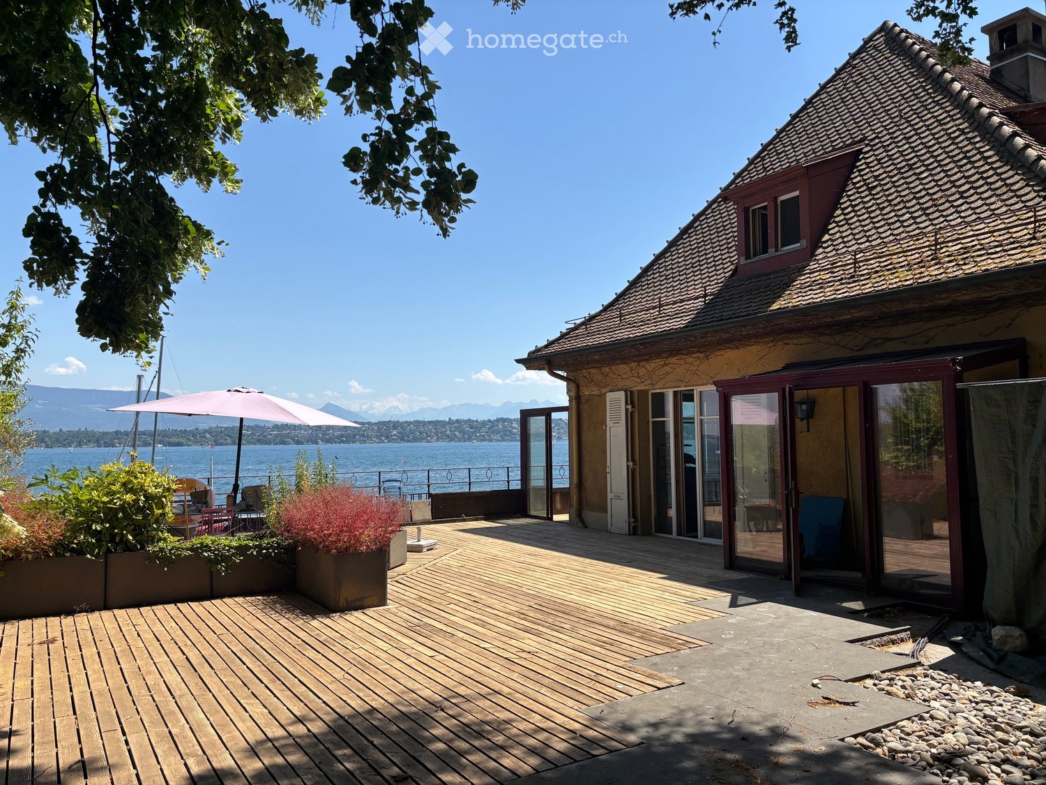 Wooden deck area with outdoor furniture, umbrella, and scenic lake view in the background.