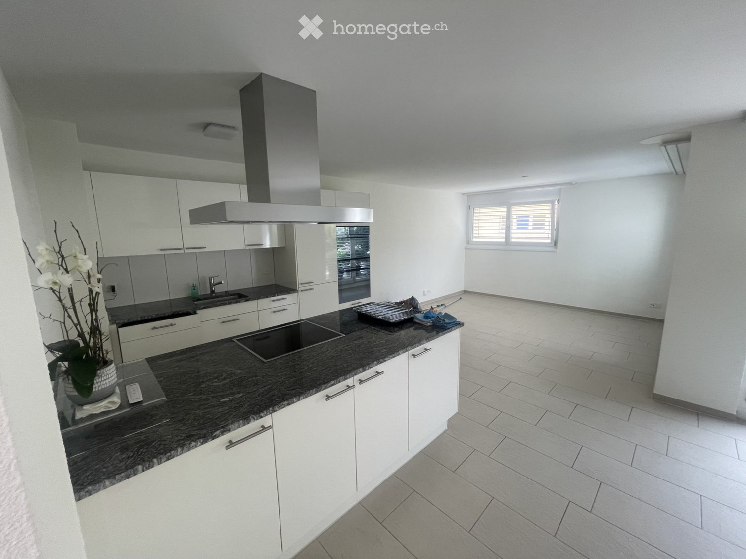 Modern kitchen with white cabinets, dark countertop, stainless steel range hood, and a window with blinds.