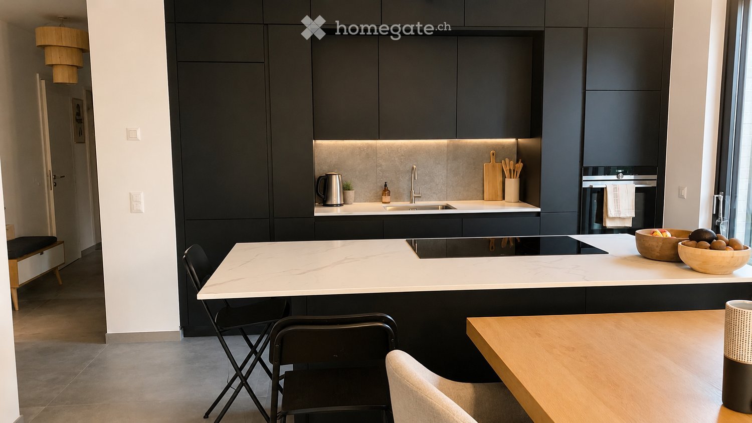 Modern kitchen with dark cabinets, white countertops, and a central island. Includes a sink, oven, and various kitchen items on the counter.