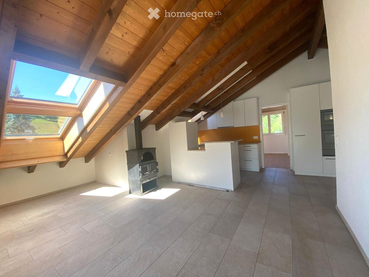 Open-plan space with a wood stove, kitchen island, and modern cabinets under a sloped wooden ceiling with skylights.