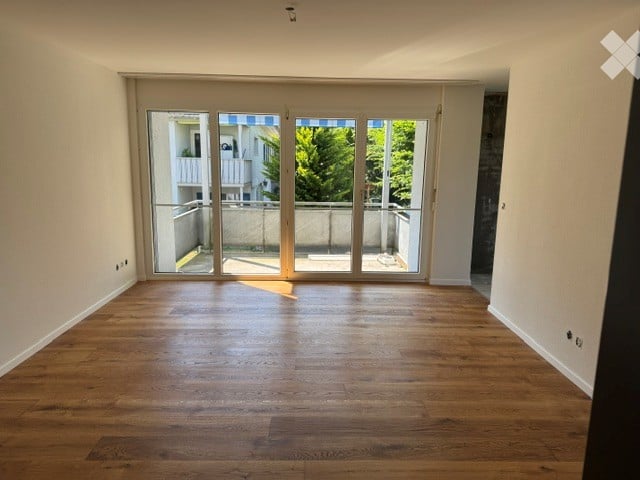 Empty room with wooden flooring and large glass sliding doors leading to a balcony.