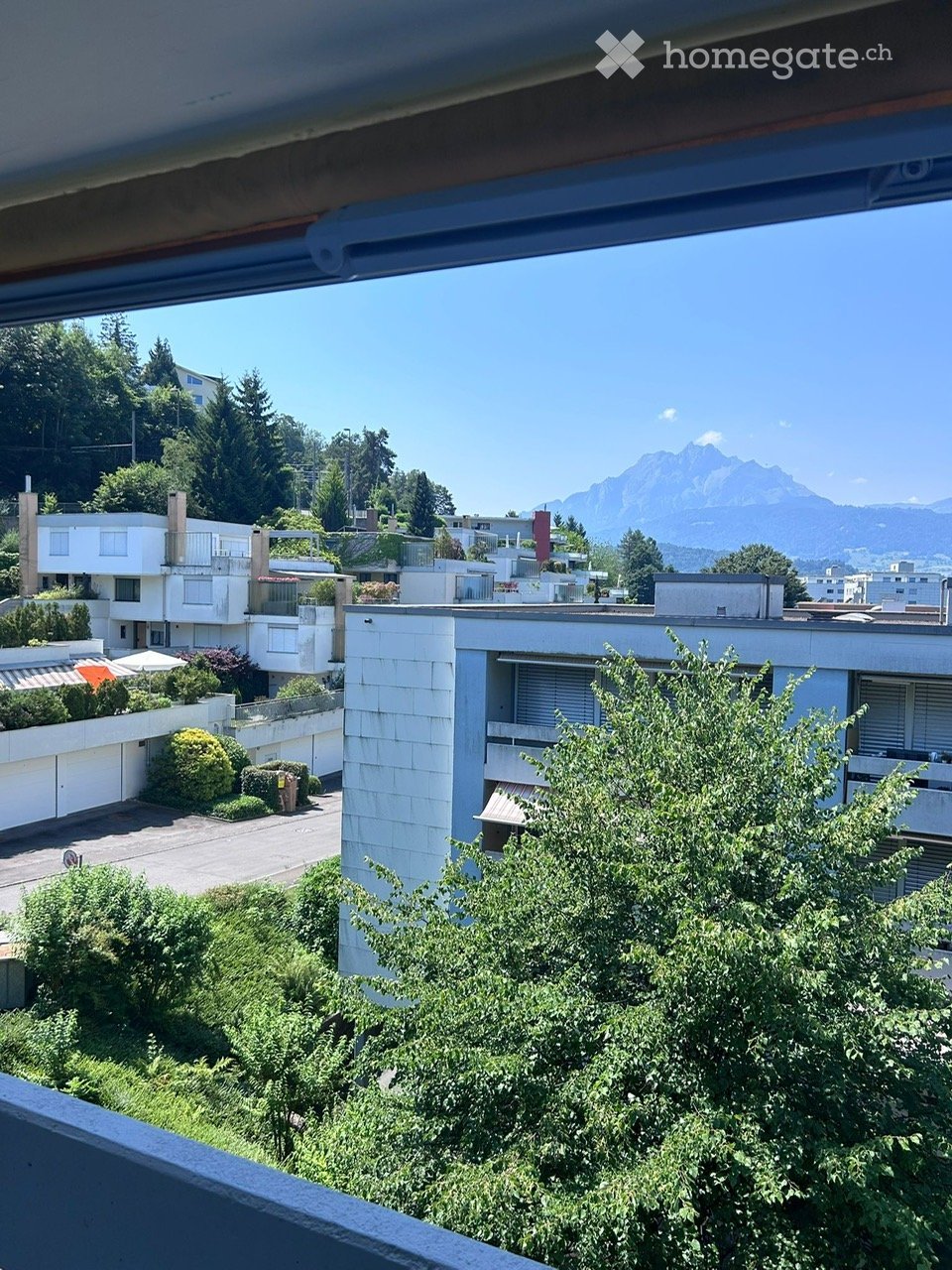 Balcony view overlooking a residential area with modern buildings, greenery, and distant mountains.
