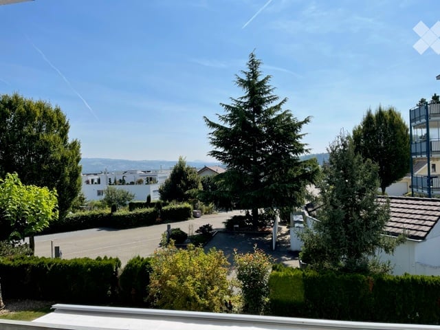 Balcony view overlooking a residential area with trees, houses, and a clear blue sky.
