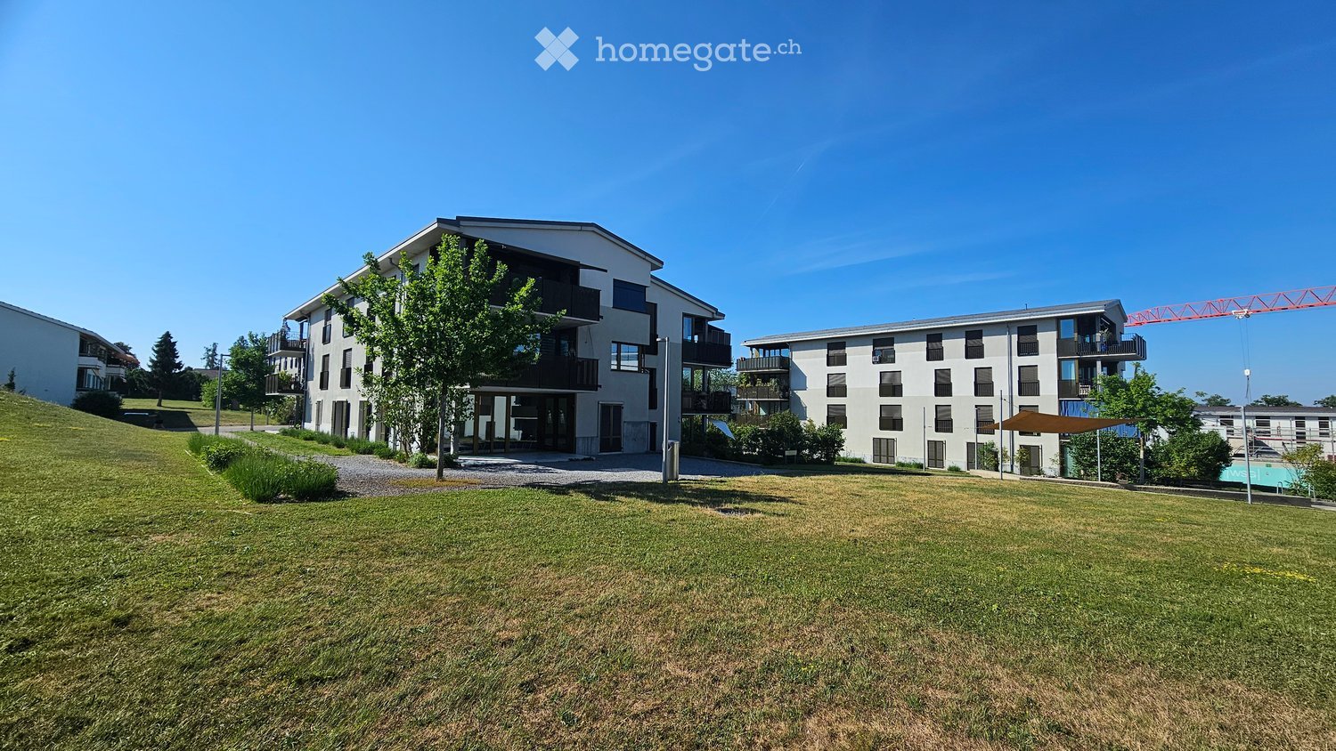 Modern multi-story residential building with balconies and large windows, surrounded by green lawn and trees.