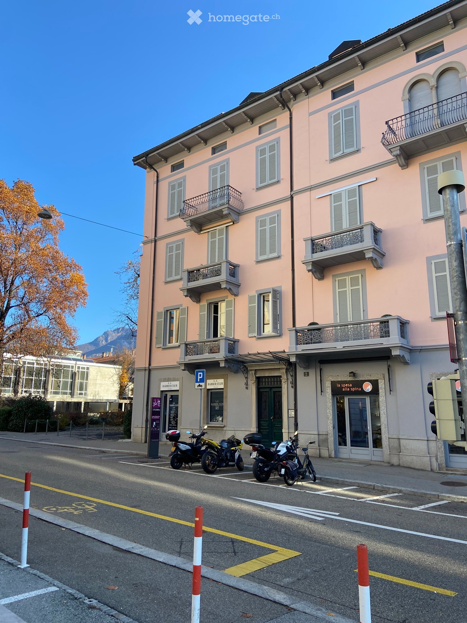 Pink multi-story building with multiple balconies and shutters, located on a street with several parked motorcycles.