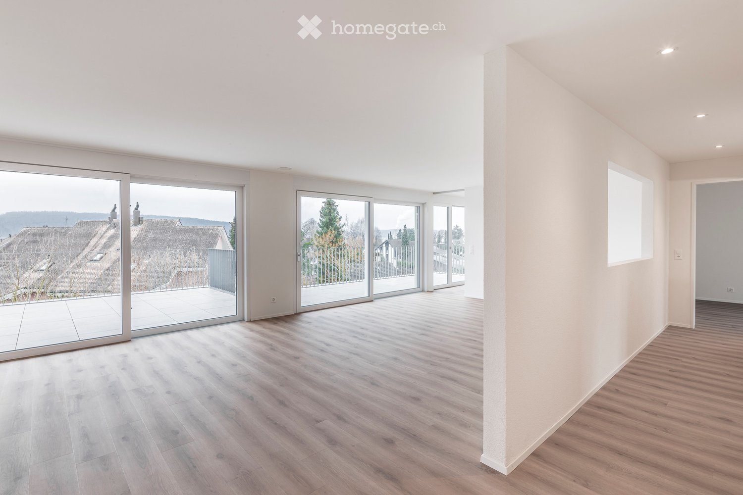 Bright, empty room with wooden flooring, large sliding glass doors leading to a balcony, and white walls.