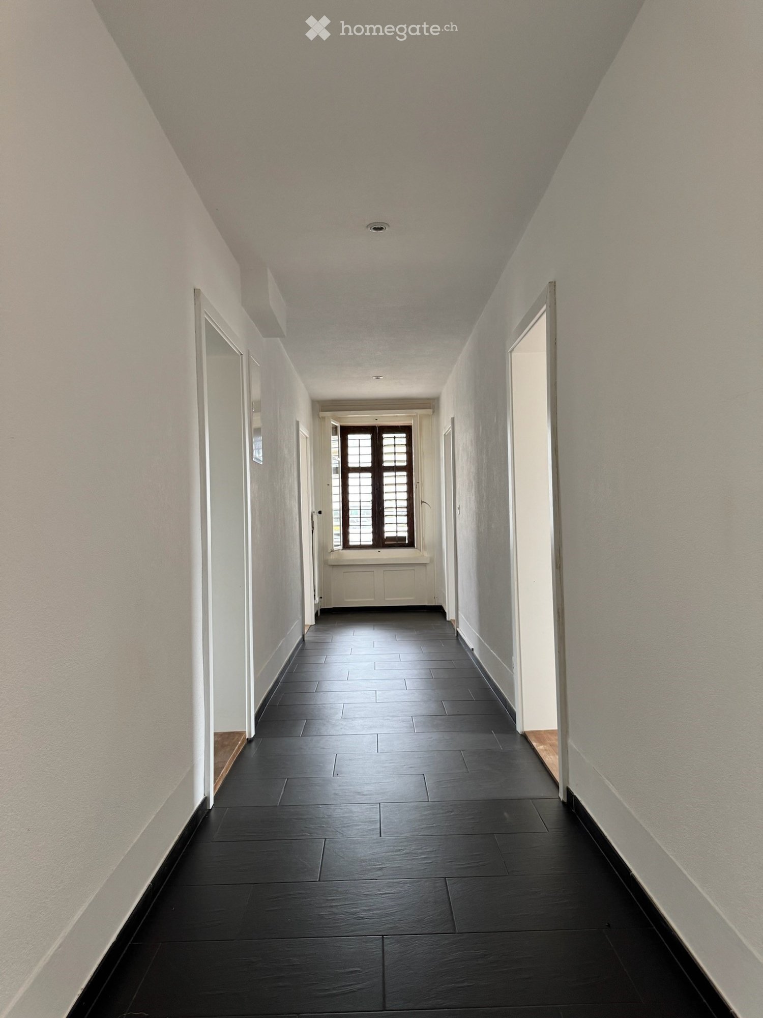 Empty hallway, white walls, black tiles, central window, white doors