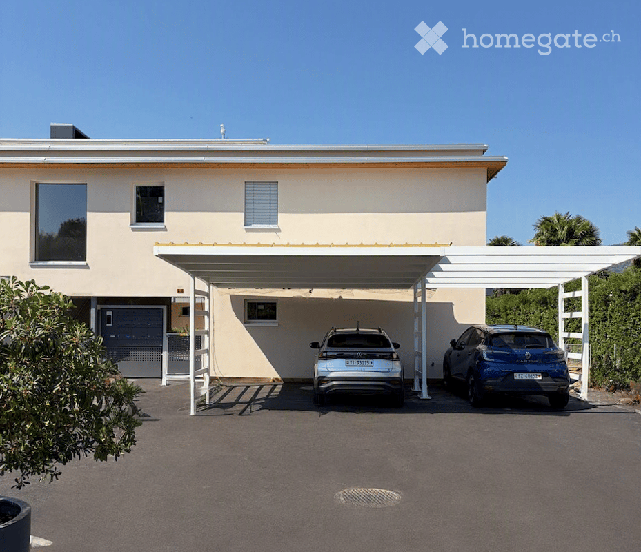 Modern single-story house with a covered parking area for two cars, featuring a clean, light-colored facade and large windows.