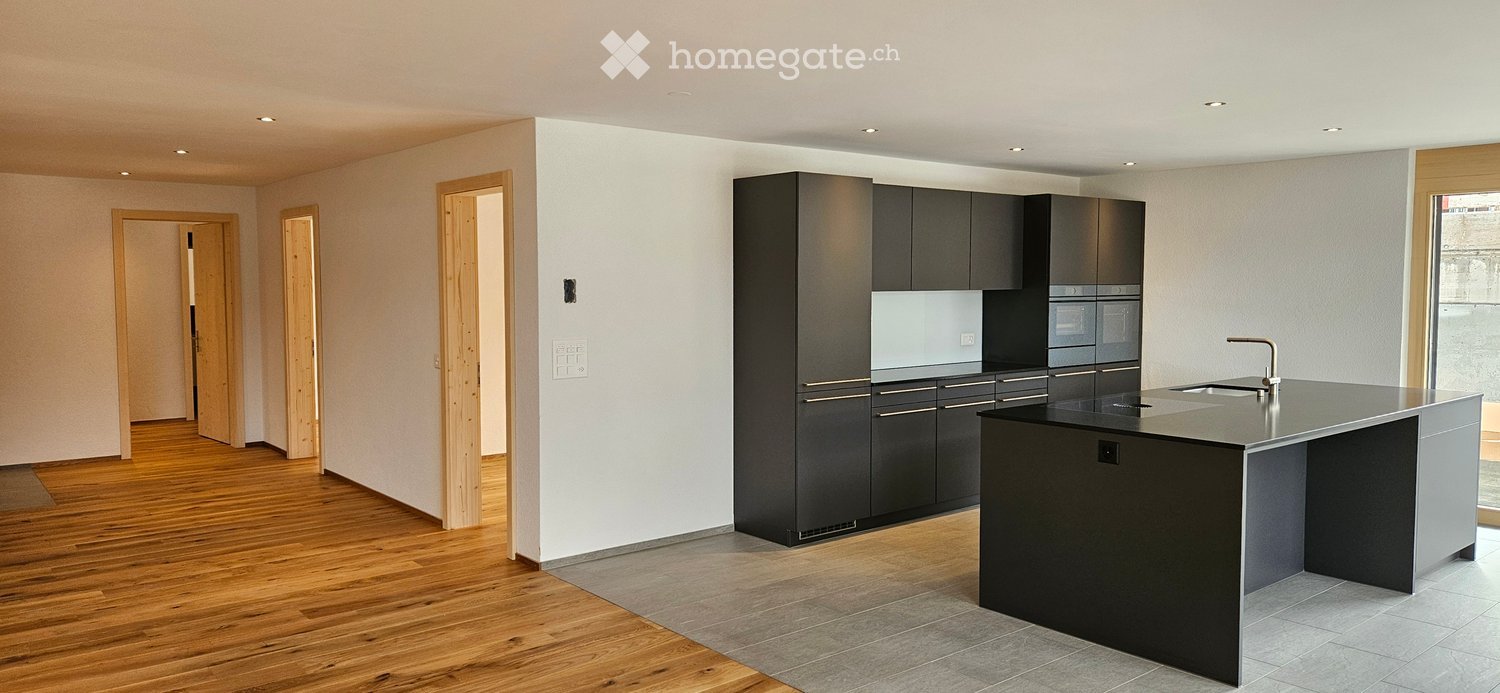 Modern kitchen with dark cabinets, a central island, and a sink, featuring wooden flooring and recessed lighting.