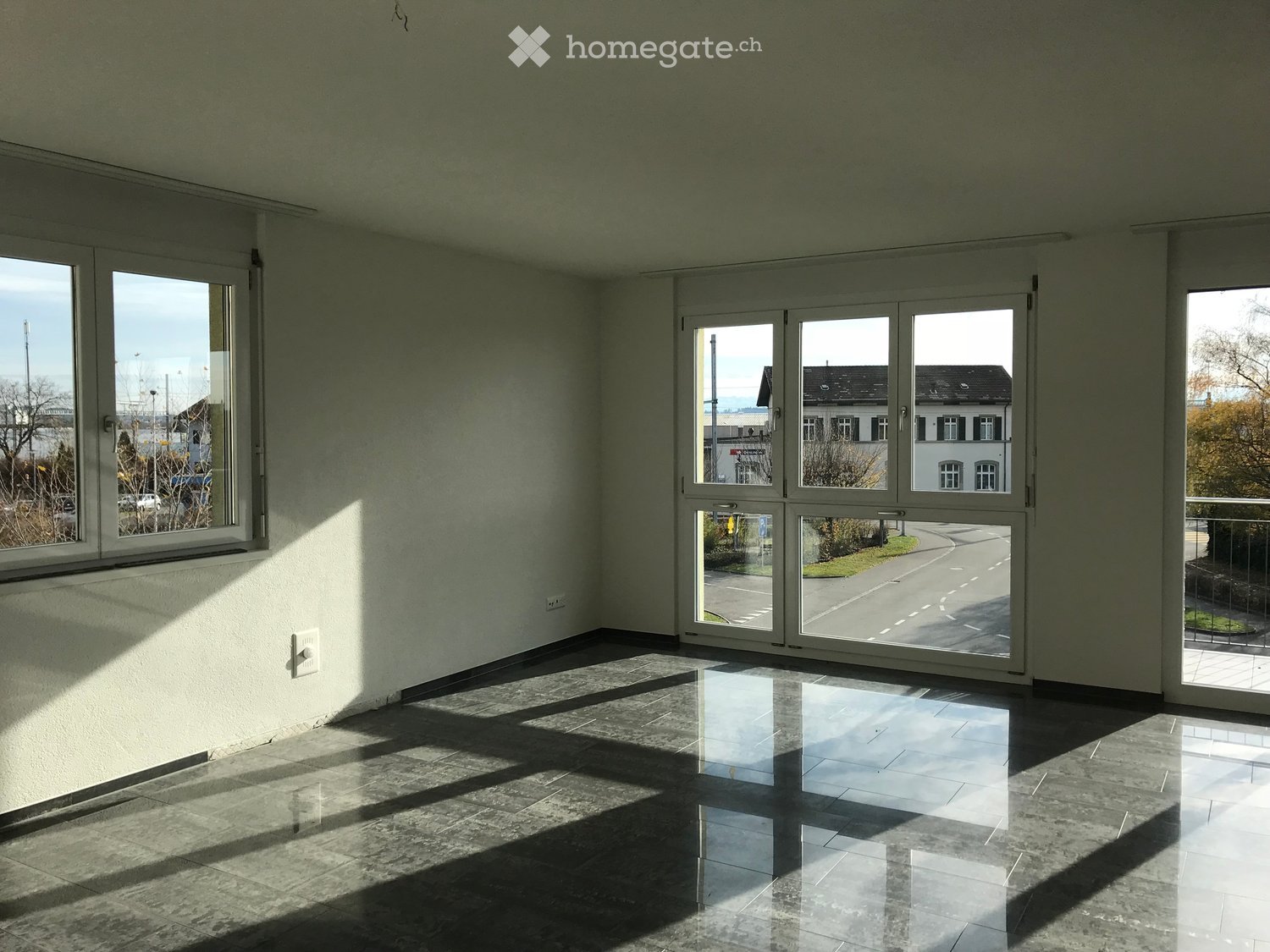 Empty room with large windows and sliding glass doors, polished tile floor, and natural light streaming in.