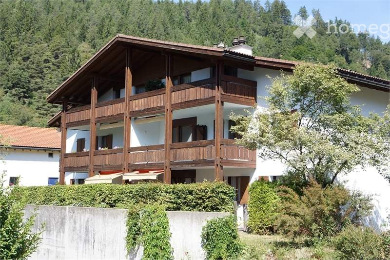 wooden balcony, brown roof, mountains in background, bushes and trees around