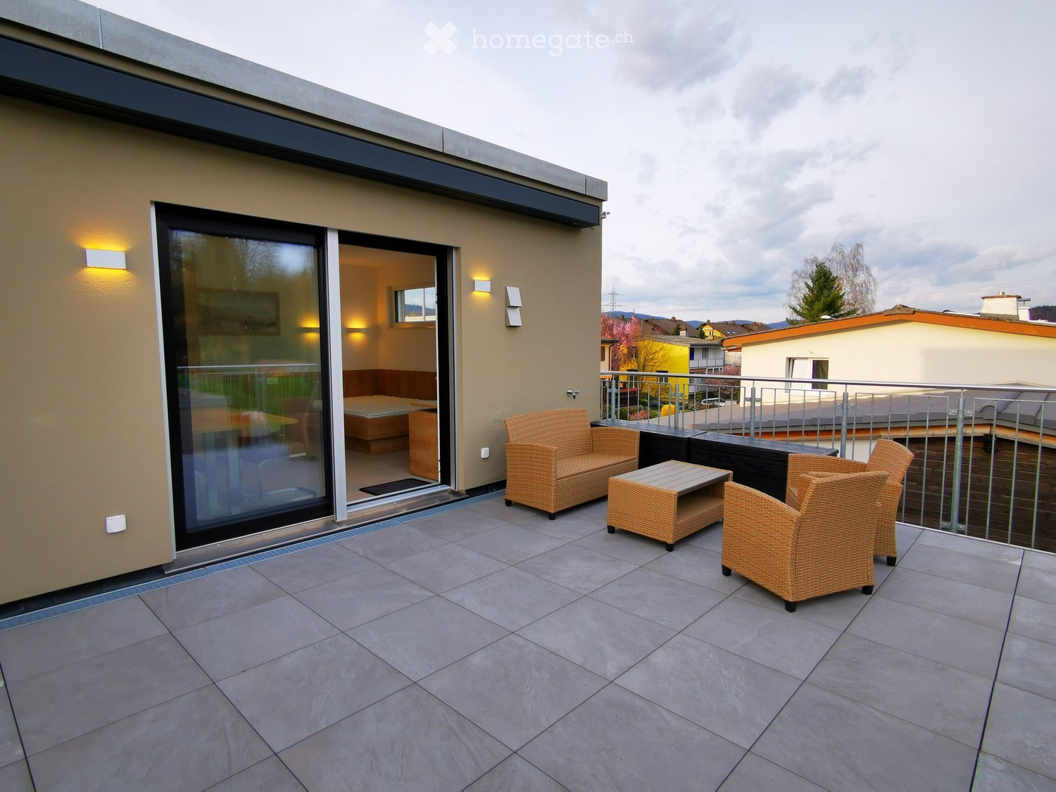 Balcony with tiled floor, modern furniture including a sofa, table, and chairs, with a view of the surrounding area.