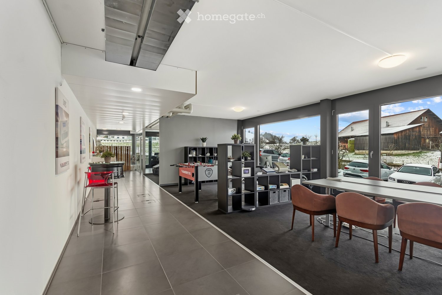 open space, bright, modern design, wooden chairs, modern table, shelves, large glass windows, foosball table, floor lamps