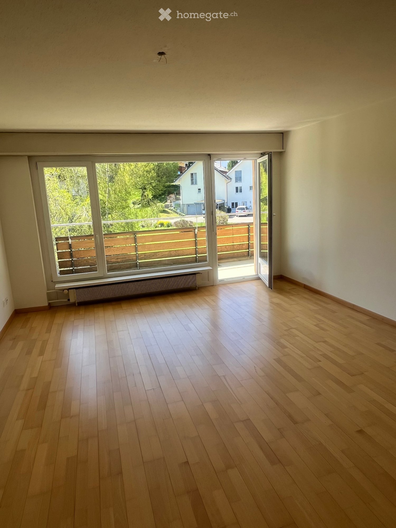 Empty room with wooden flooring, large windows, and a sliding glass door leading to a balcony area.