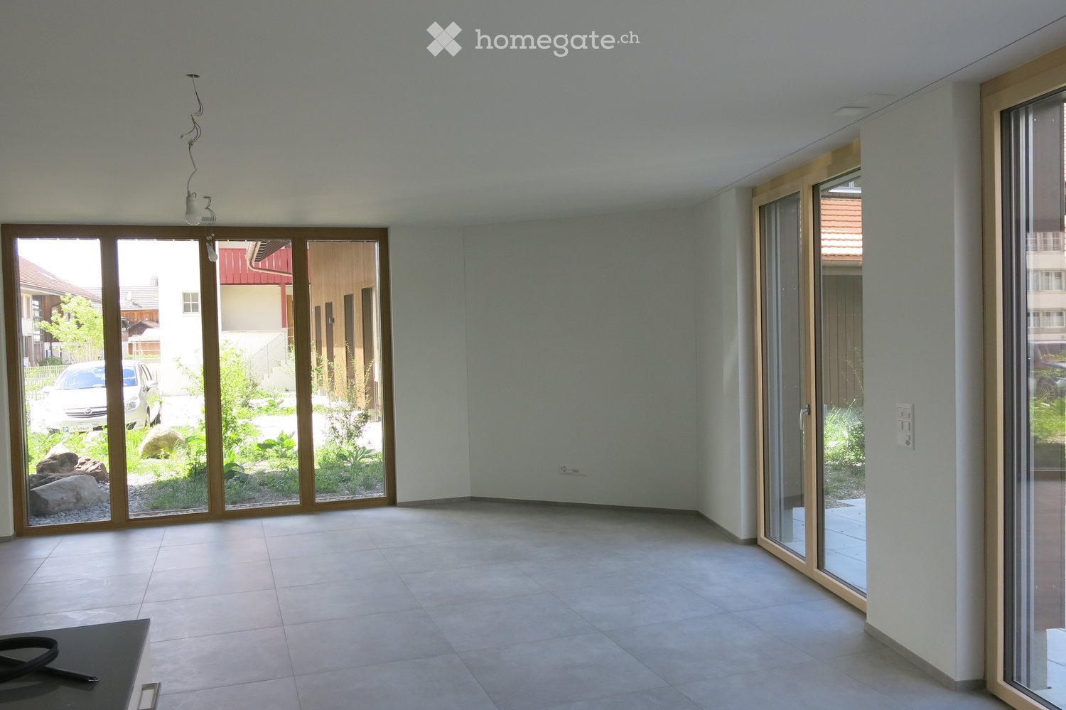 Empty room with large sliding glass doors leading to a garden, tiled floor, and white walls.