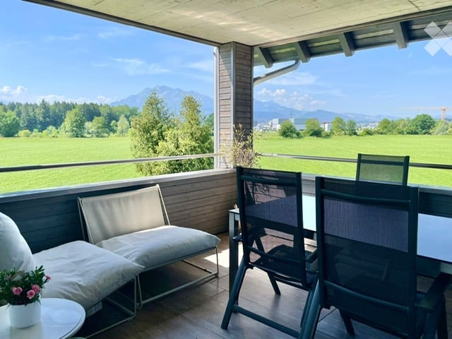 Balcony with outdoor seating area, overlooking a green field and mountains.