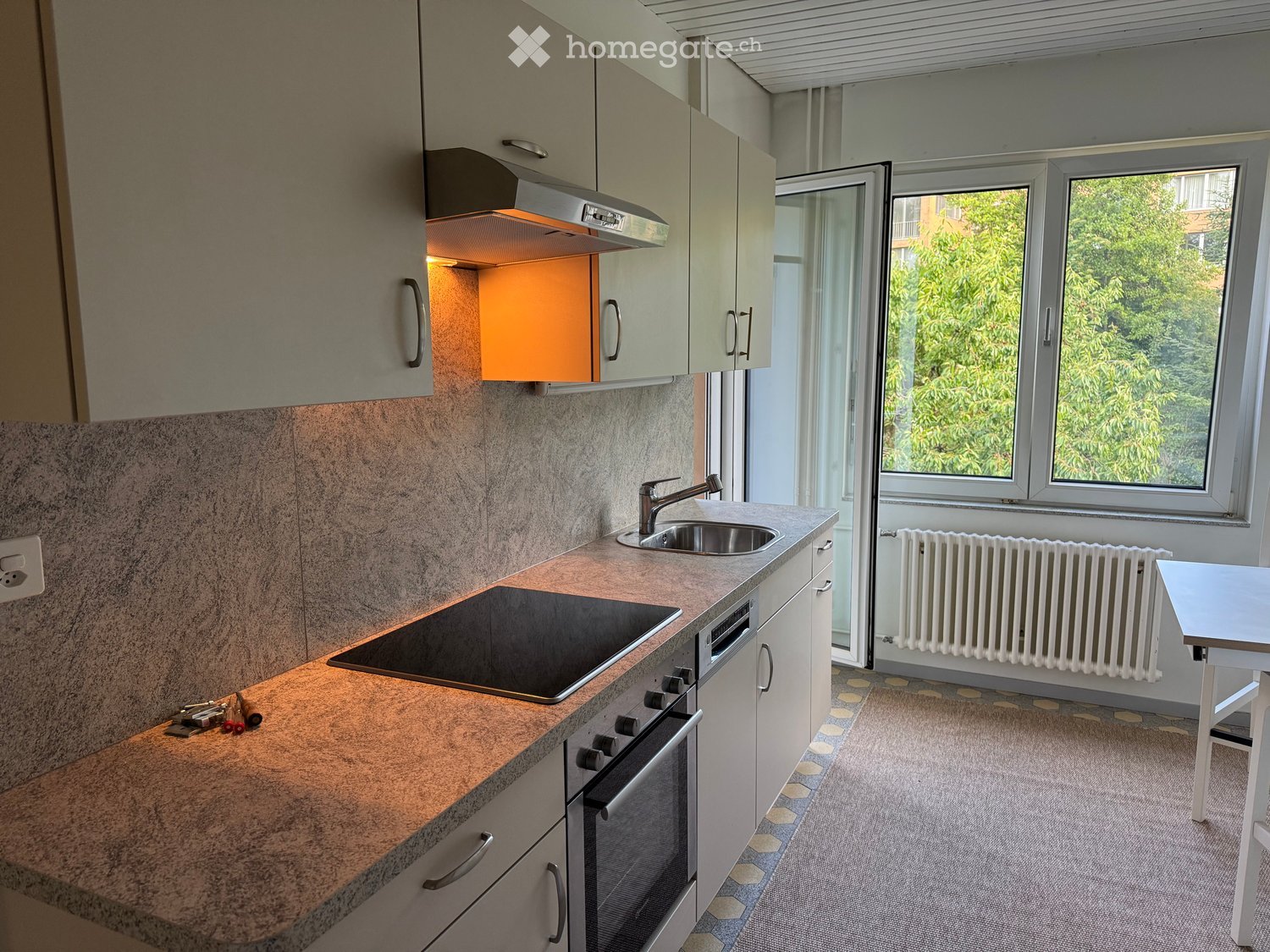 Modern kitchen with light-colored cabinets, granite countertop, built-in stove, sink, and radiator near the window.