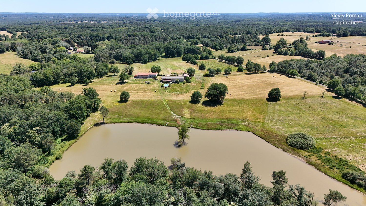 Aerial view of a rural property with fields, trees, a pond, and several buildings including a house and barn.