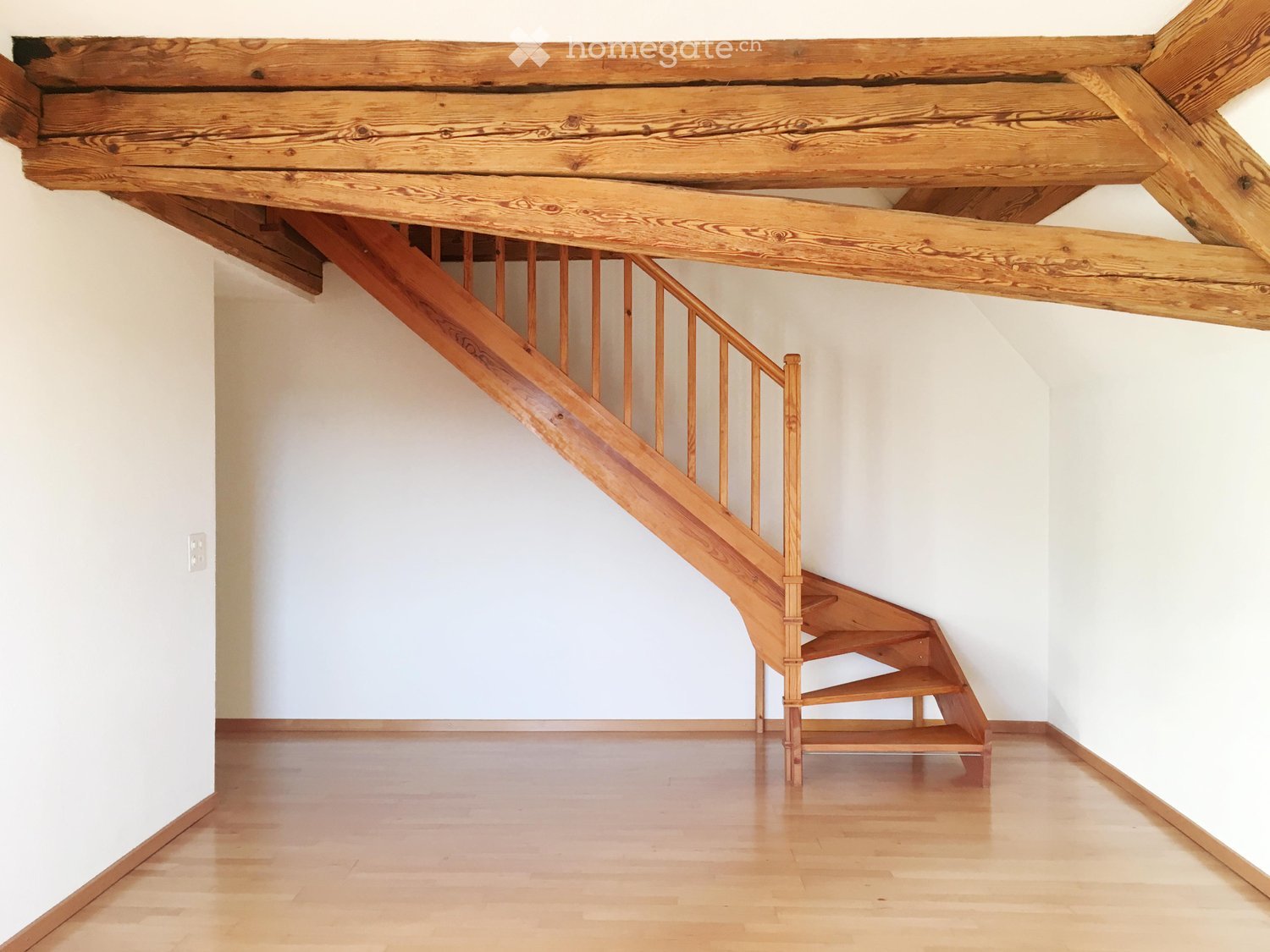 Empty hallway with wooden staircase leading to an upper level, light-colored walls, and polished wooden floor.