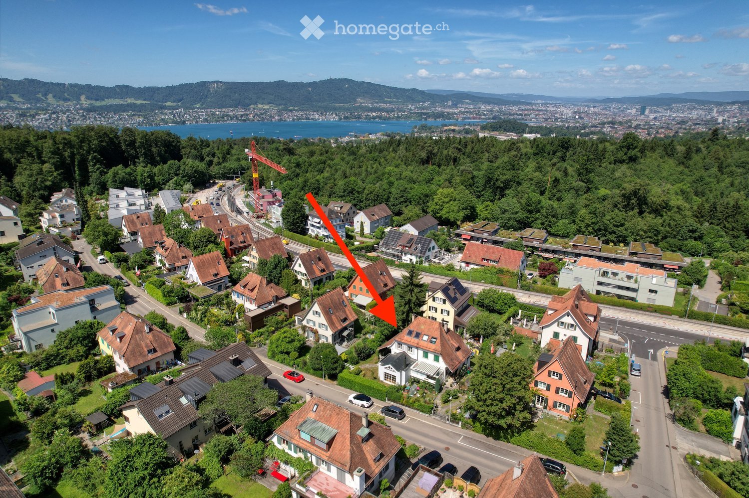 Aerial view of a residential neighborhood with multiple houses, surrounded by greenery and a body of water in the background.