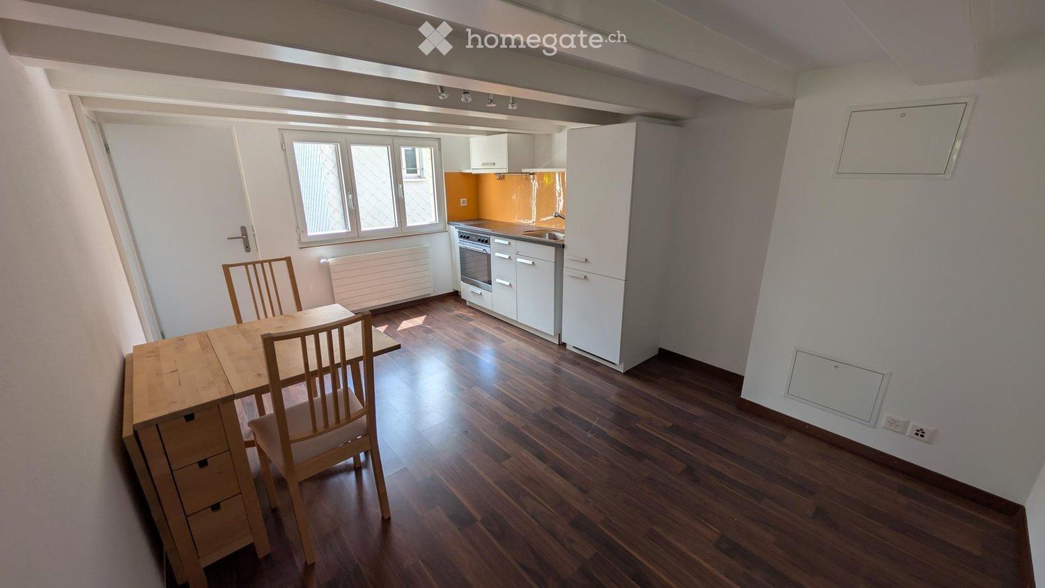 A modern, well-lit kitchen and dining area with wooden flooring, white cabinets, and a small dining set.