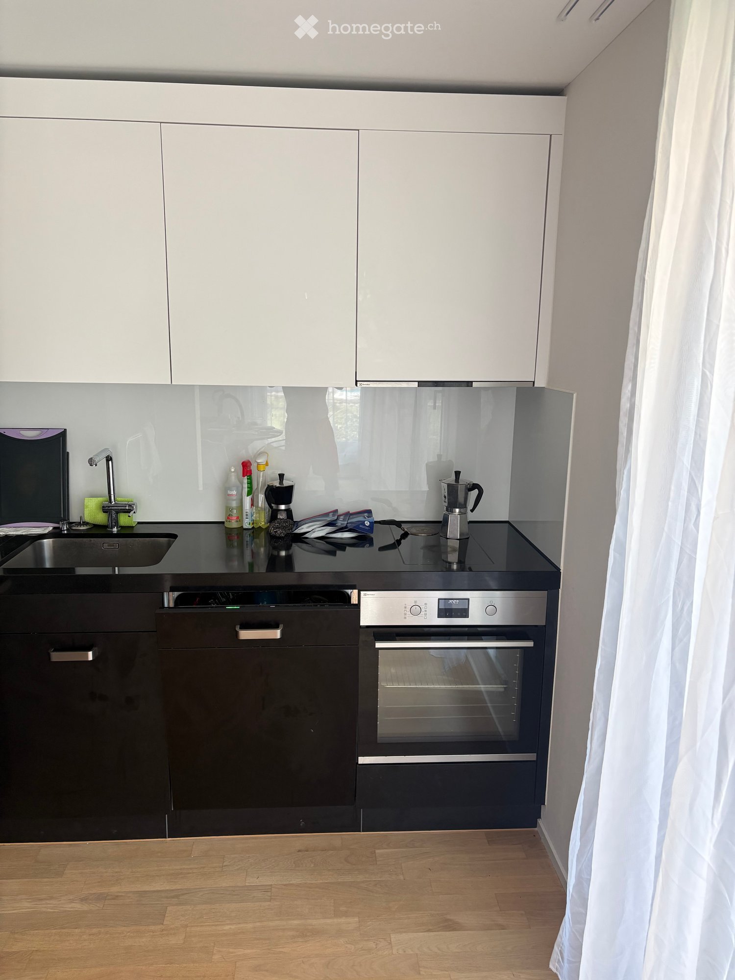 Modern kitchen with white cabinets, black countertops, stainless steel appliances, and wooden flooring.