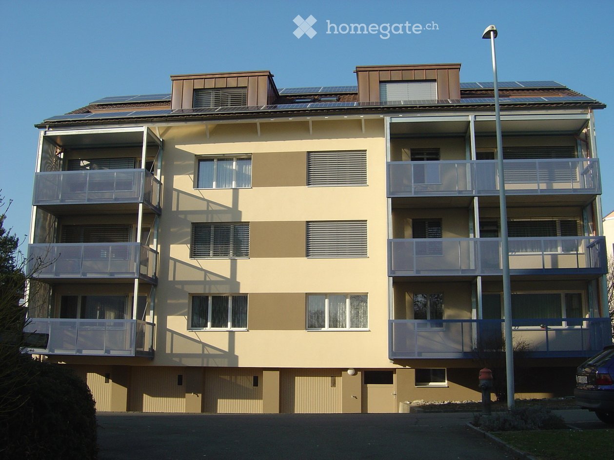 Four-story residential building with balconies, solar panels on the roof, and a modern facade.