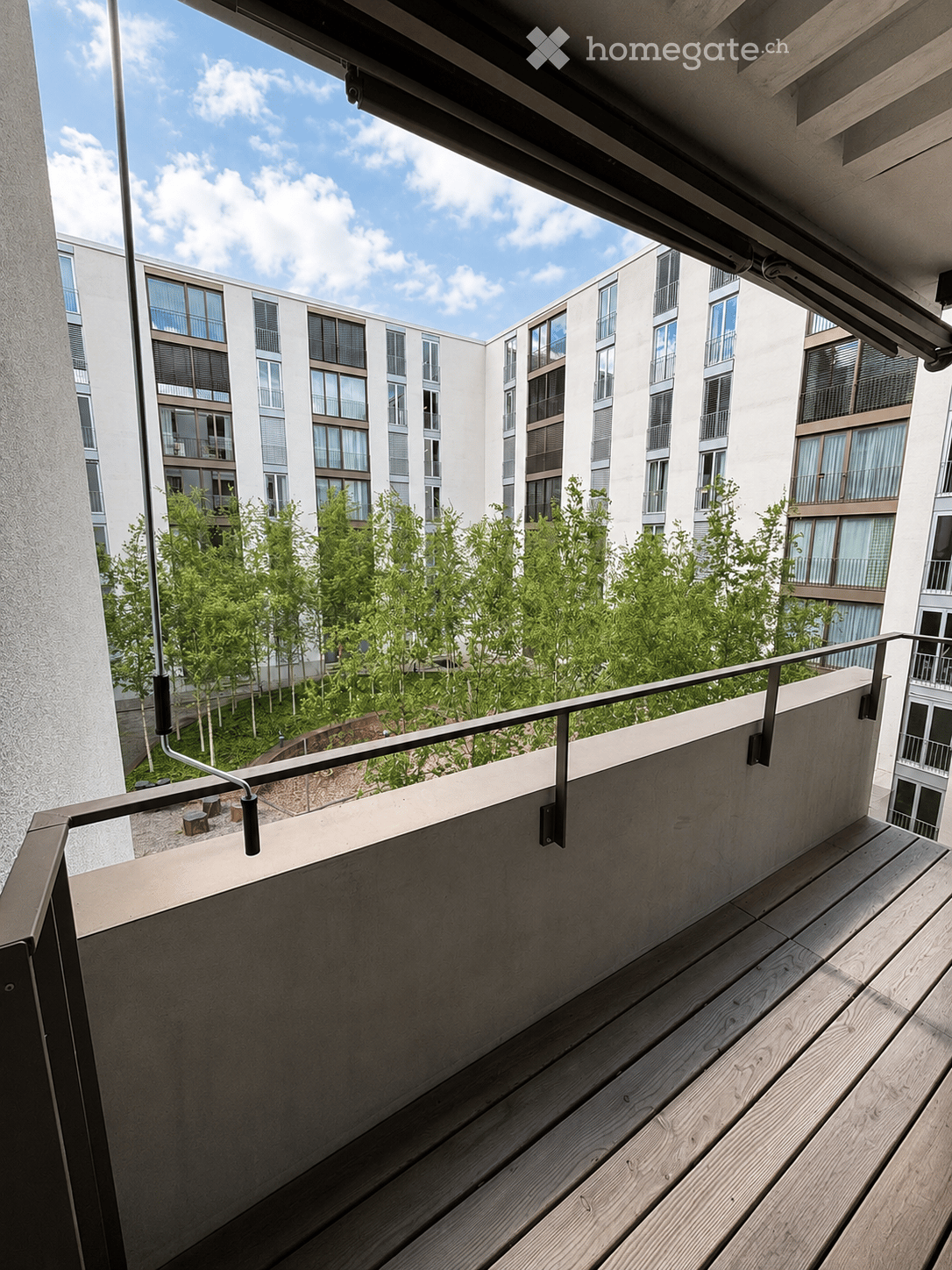Balcony with wooden decking, metal railing, and a view of a modern residential building and greenery.