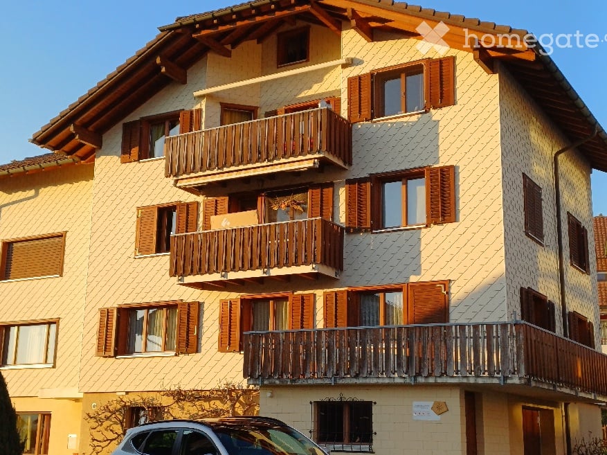 Multi-story residential building with wooden balconies, large windows, and brown shutters.