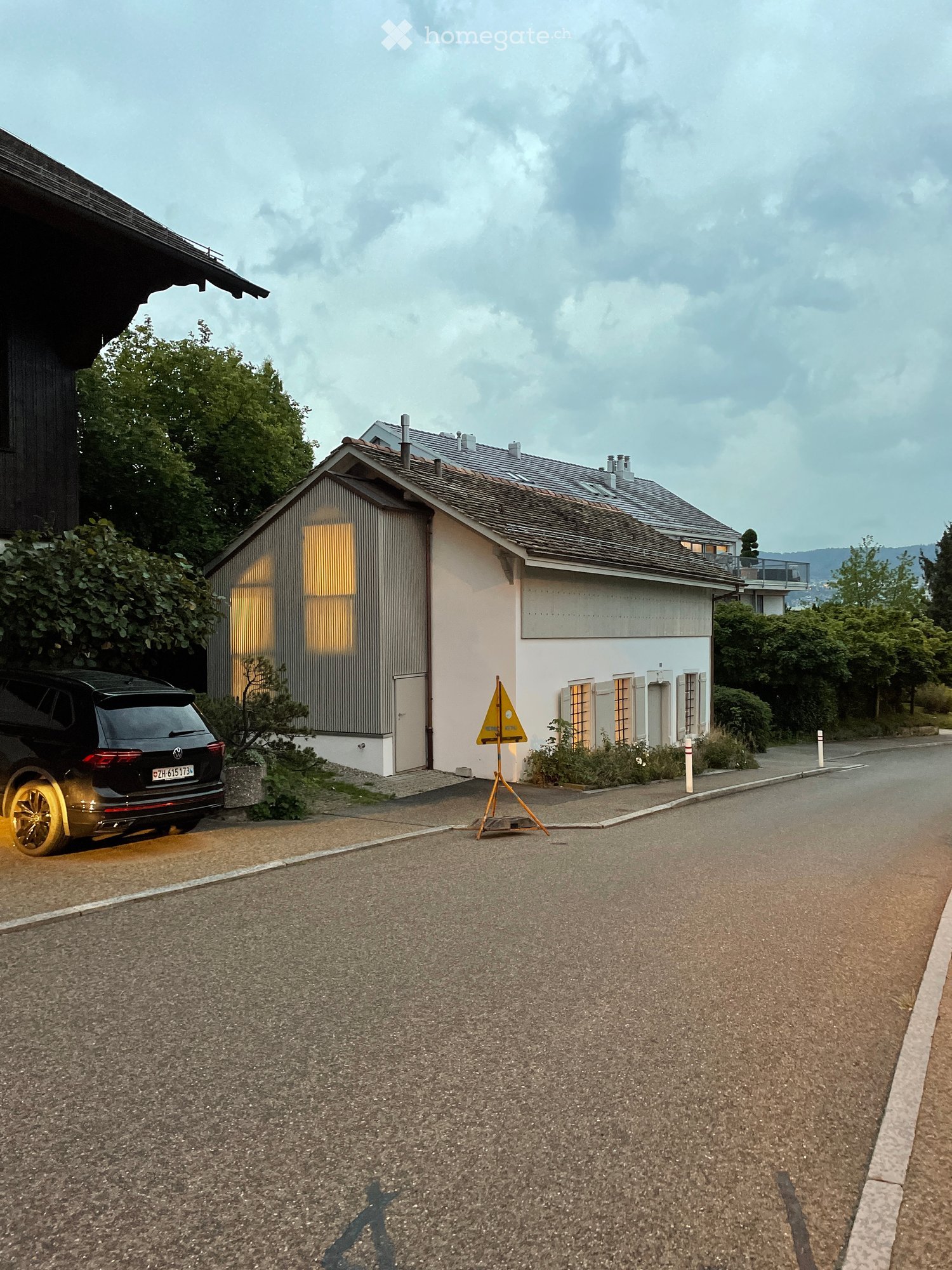 Two-story house with a modern design, featuring a garage and a parked car with yellow wheels.