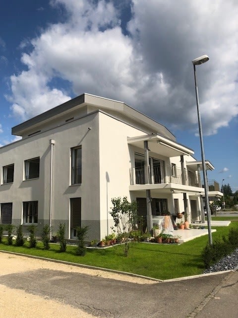 Modern two-story house with white exterior, large windows, and a balcony on the upper floor.
