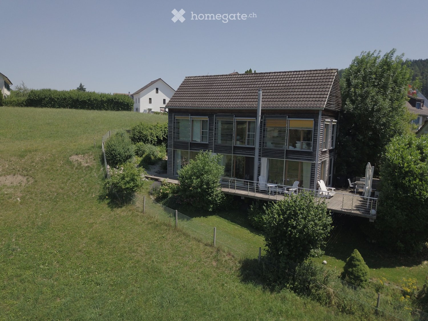 Two-story house with a modern design, featuring large windows, a balcony, and a well-maintained lawn.