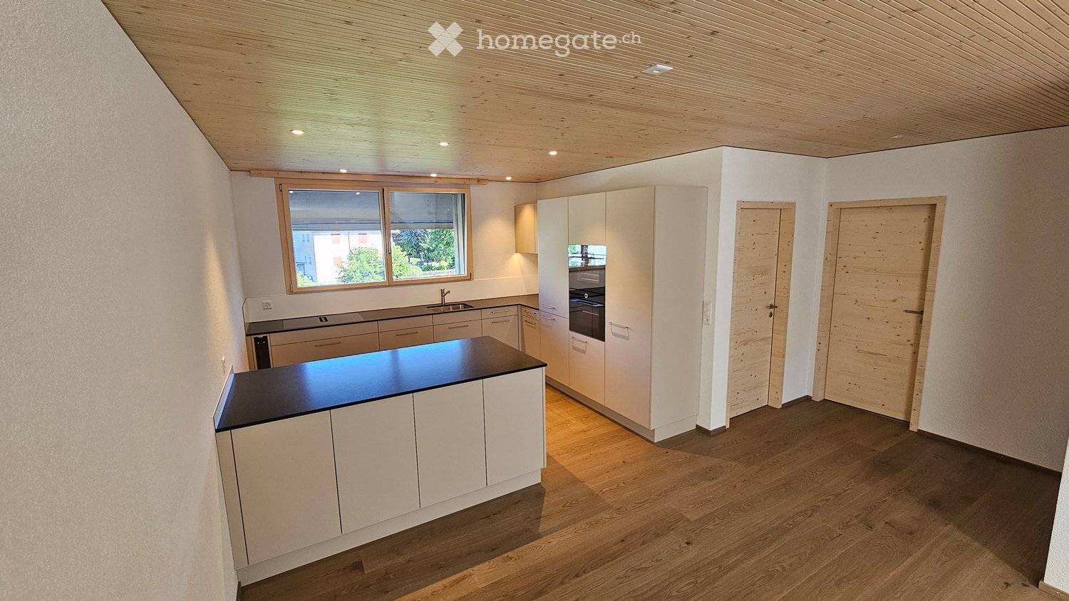 Modern kitchen with white cabinets, dark countertop, wooden flooring, and large window offering a view.